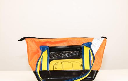 Left side of bag. Black and Orange with black zipped pocket and life raft feature. 